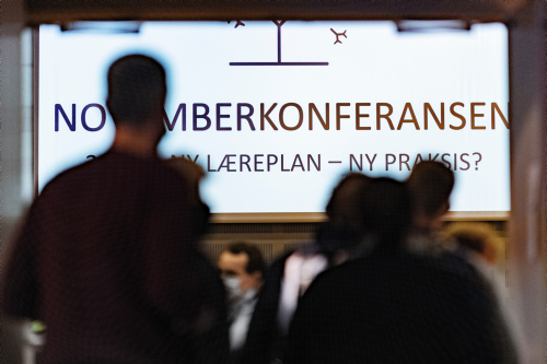 Logoen til Novemberkonferansen 2021 vises på skjerm med noen personer foran