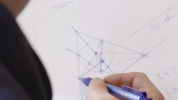 VI ser noen som tegner en geometrisk figur på et hvitt ark.