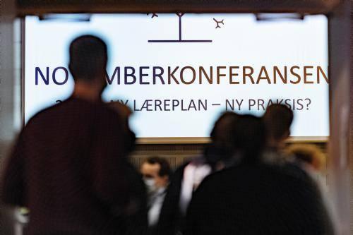 En plakat med "Novemberkonferansen" sees i bakgrunnen, foran ser vi skyggen av to personer.