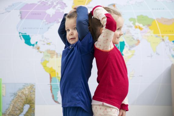 Bilde av jente og gutt på ca. tre år, som måler lengde foran et verdenskart