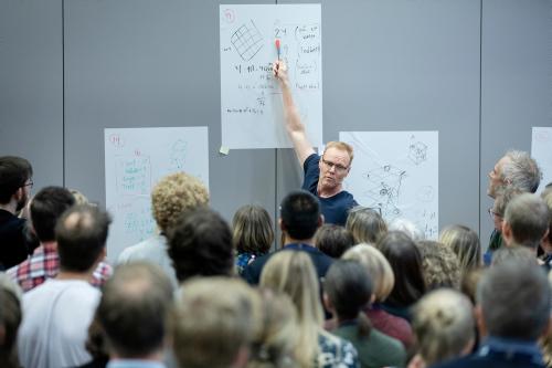 Mann som står foran en gruppe mennesker og peker på en av tre whiteboard-tavler som henger bak ham. Mannen heter Peter Liljedahl.