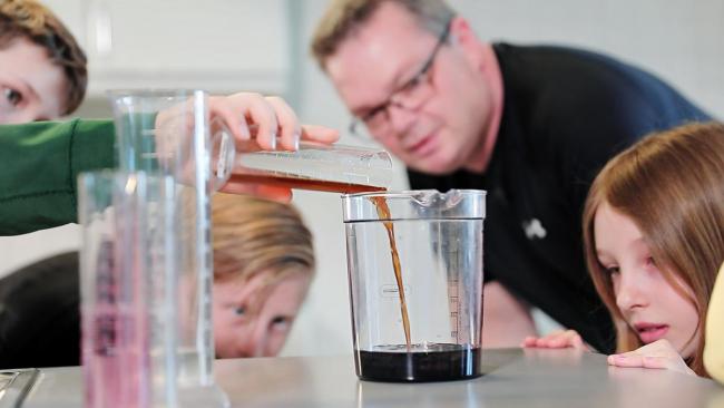 Lærer og tre elever som heller brun væske fra reagensrør over i et glass
