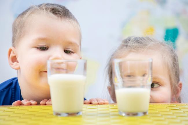 To små barn som sammenligner mengde melk i to melkeglass. 