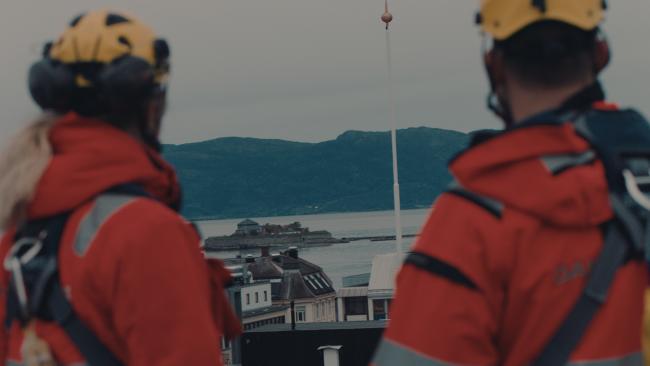 To arbeidere på et tak kikker utover Trondheimsfjorden mot Munkholmen