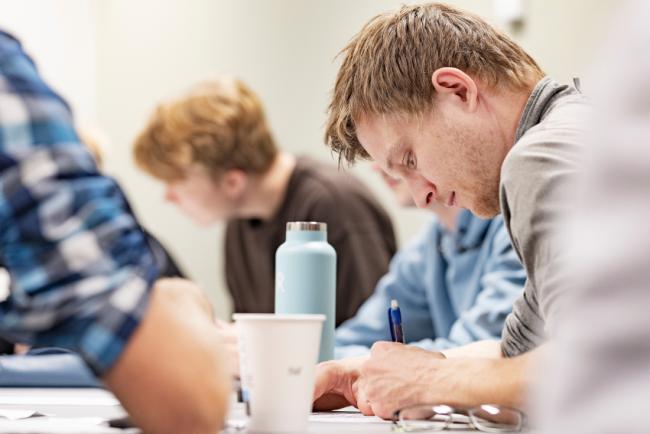 Student som leser ved en pult. Andre studenter synes i bakgrunnen.