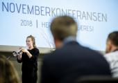 Jente som spiller trompet - åpner Novemberkonferansen. I forgrunnen ser vi bakhodet på en mann og bak musikeren, en skjerm med logoen til Novemberkonferansen. 