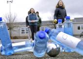 Elever som kaster en metallkule på plastikkflasker utendørs
