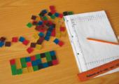 Bilde av elevarbeid med kvadratiske tellebrikker og en tabell